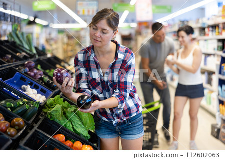 Portrait of cheerful female customer taking fresh eggplant on supermarket 112602063