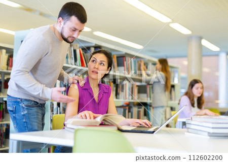 Students in the library are studying on a laptop and looking for information in books Students in the library are studying on a laptop and looking for information in books 112602200