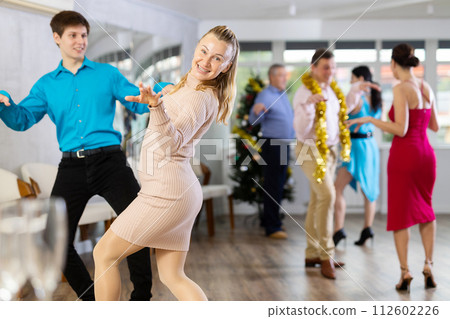 Cheerful woman dancing twist paired with young colleague at New Year party 112602226