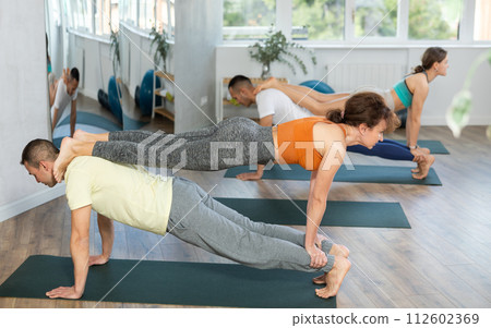 Young couple practicing acro yoga on mat with group of sporty people in yoga studio Young couple practicing acro yoga on mat with group of sporty people in yoga studio 112602369