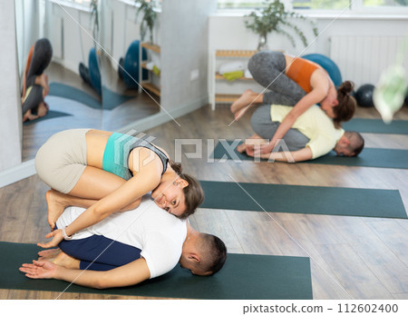 Young couple practicing acro yoga on mat in studio together, flexibility class workout Young couple practicing acro yoga on mat in studio together, flexibility class workout 112602400