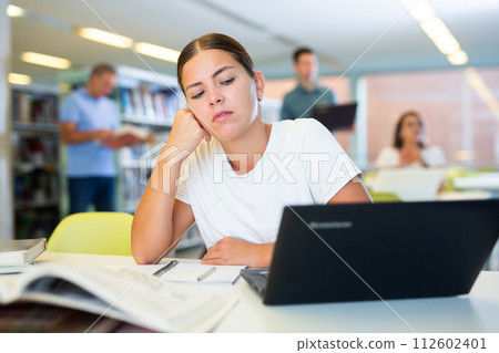 Portrait of upset tired female student in library 112602401