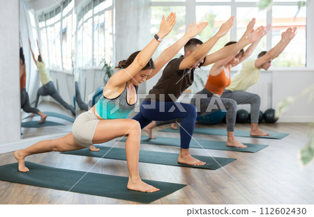 Happy woman standing yoga pose and making full body stretching workout with group people in sports room 112602430