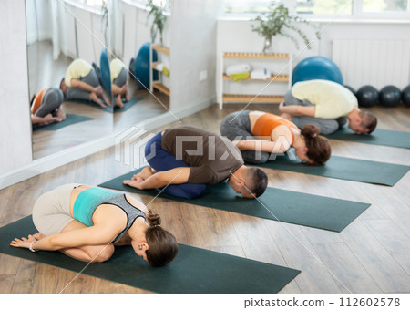 Lovers of active lifestyle on yoga mat perform doing version of child pose in gym Lovers of active lifestyle on yoga mat perform doing version of child pose in gym 112602578