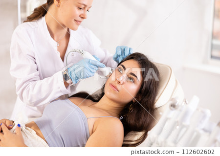 Brunette girl having facial beauty massage by European female aesthetician (vabration import) 112602602