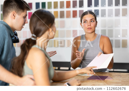 Female saleswoman of paintwork material shop advises spouses buyer with samples and product catalog Female saleswoman of paintwork material shop advises spouses buyer with samples and product catalog 112602676