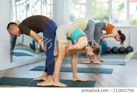 Acroyoga, two sporty people practice yoga in pair, couple doing stretching exercise standing pose half forward bend at yoga club Acroyoga, two sporty people practice yoga in pair, couple doing stretching exercise standing pose half forward bend at yoga club 112602706