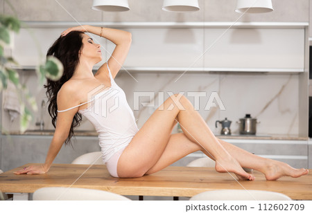 Beautiful woman in top and panties poses erotically on the table of modern kitchen 112602709