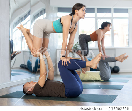 Multiethnic group of sporty people practicing various partner yoga positions during training in fitness gym, couple acro yoga Multiethnic group of sporty people practicing various partner yoga positions during training in fitness gym, couple acro yoga 112602756