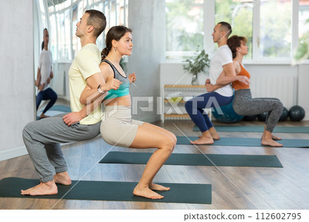 Women and men who want to maintain a healthy lifestyle practicing yoga with others during group lessons in gym Women and men who want to maintain a healthy lifestyle practicing yoga with others during group lessons in gym 112602795