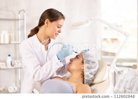 Aesthetician administering facial procedure on woman using ion bubble attachment 112602848