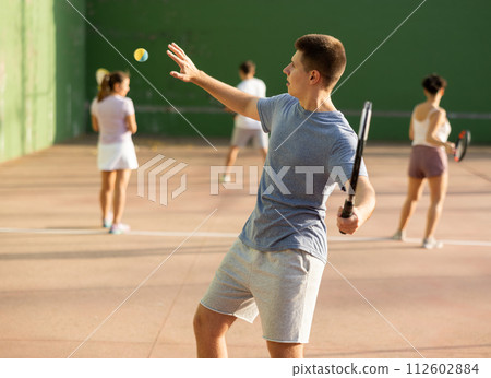 Young frontenis player swinging racquet to hit ball on outdoor court 112602884