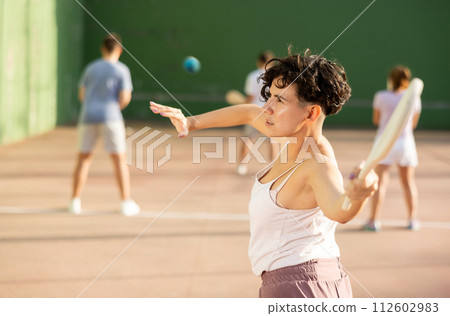 Portrait of sporty girl playing paleta fronton on outdoor court, ready to hit ball. Healthy and active lifestyle concept Portrait of sporty girl playing paleta fronton on outdoor court, ready to hit ball. Healthy and active lifestyle concept 112602983