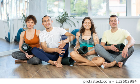Happy portrait of four young people posing with mats, going to practicing yoga at gym 112602984