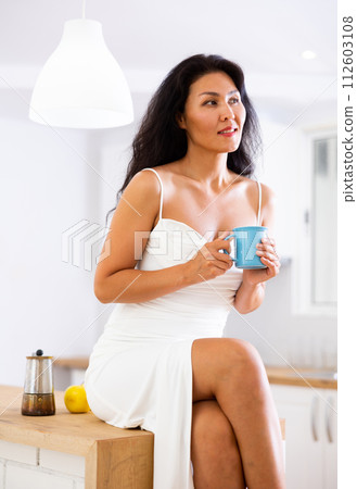 Attractive woman in nightgown drinking hot drink at home Attractive woman in nightgown drinking hot drink at home 112603108