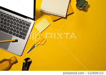 Top view of laptop with empty display, water bottle and office supplies on yellow background 112606113