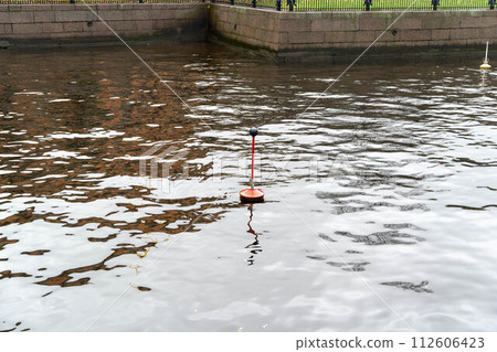 A weathered nautical hanger sign displaying navigational information on an urban river, serving as a vital guide for boats with the cityscape in the background. 112606423