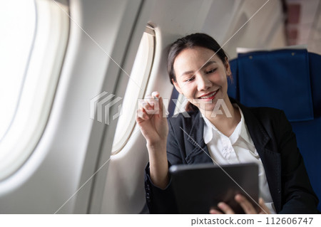 Smiling happy business woman asian flying and working in an airplane in first class, Woman sitting inside an airplane using digital tablet 112606747