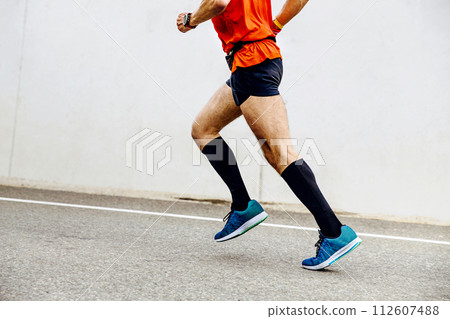 side view man running in black compression socks in background white concrete wall side view man running in black compression socks in background white concrete wall 112607488