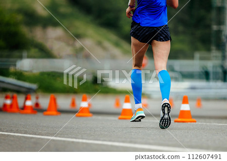 close up women legs running down road with orange safety cones, blue compression sleeves close up women legs running down road with orange safety cones, blue compression sleeves 112607491
