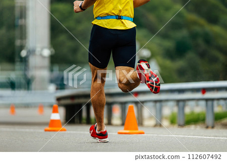 close up man legs running down road with orange safety cones 112607492