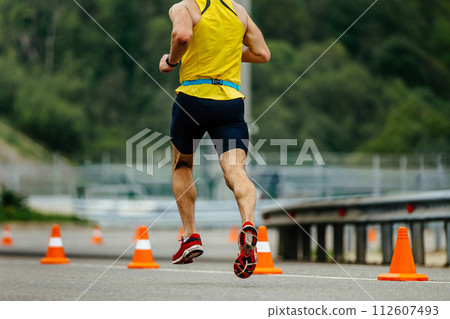 back male athlete running on asphalt with orange safety cones, mountain marathon race back male athlete running on asphalt with orange safety cones, mountain marathon race 112607493