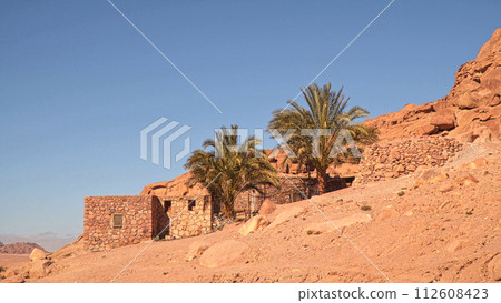 A small building and palm trees on the slope of the desert mountains 112608423