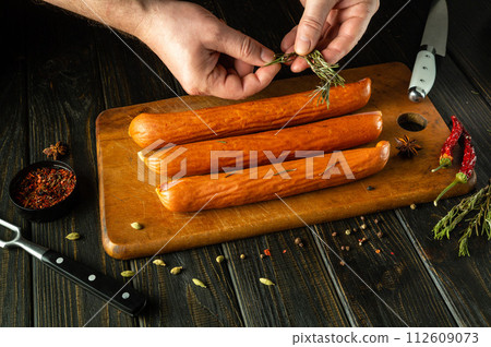 Cooking aromatic sausage on the kitchen table with the hands of a chef. Add rosemary to meat sausages before grilling. Low key concept of serving delicious lunch Cooking aromatic sausage on the kitchen table with the hands of a chef. Add rosemary to meat sausages before grilling. Low key concept of serving delicious lunch 112609073