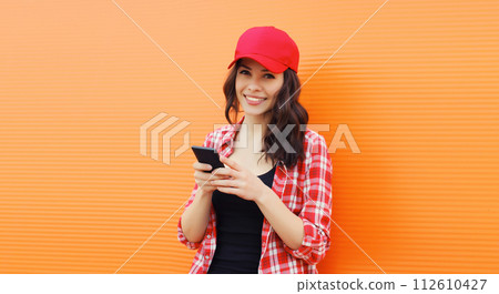 Portrait of happy smiling young woman with mobile phone on colorful orange background 112610427