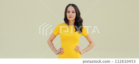 Beautiful young brunette woman model posing in yellow dress on city street Beautiful young brunette woman model posing in yellow dress on city street 112610453
