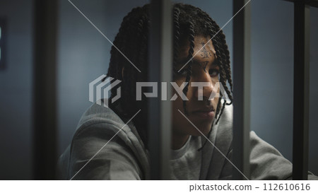African American young criminal stands in prison cell and looks at camera 112610616
