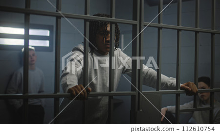 Multiethnic teenagers behind metal bars in prison cell look at camera Multiethnic teenagers behind metal bars in prison cell look at camera 112610754