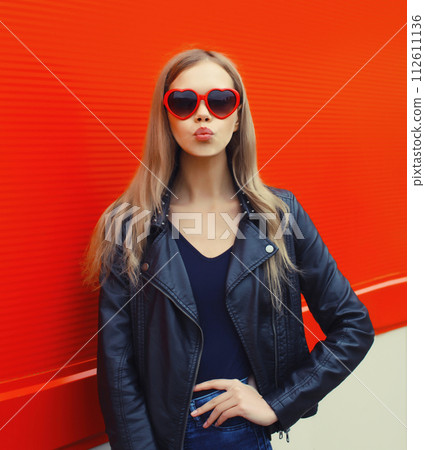 Portrait of beautiful stylish blonde young woman model blowing kiss in red heart shaped sunglasses 112611136