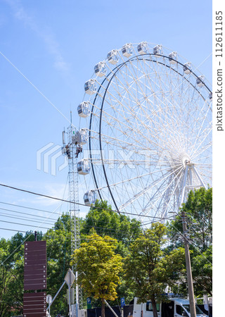 Workers on a communication tower by a ferris wheel in white color against summer blue sky 112611185