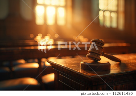 Warm sunlight bathes a courtroom, highlighting a judge's gavel on the bench 112611480