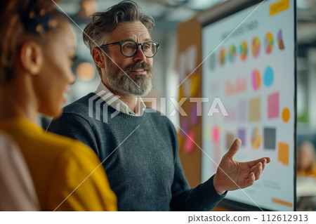 Professional male presenting a strategy to a female colleague near a board with graphs 112612913