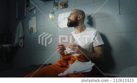 Criminal looks at family photos and kids drawings in prison cell Criminal looks at family photos and kids drawings in prison cell 112613323