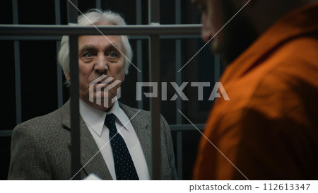 Lawyer talks with inmate standing in prison cell, offers his services 112613347