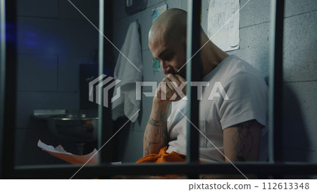 Male prisoner looks at his child drawings and cries sitting on bed in prison cell Male prisoner looks at his child drawings and cries sitting on bed in prison cell 112613348