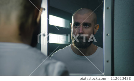 Male inmate wipes his face with towel and looks aggressively in the mirror Male inmate wipes his face with towel and looks aggressively in the mirror 112613428
