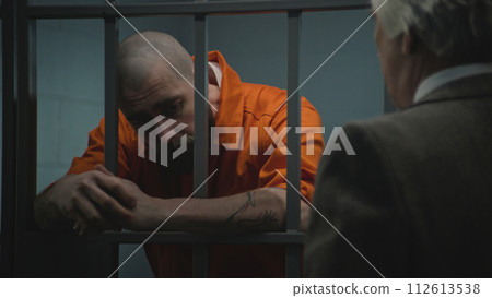 Prisoner in uniform stands in prison cell, talks with lawyer Prisoner in uniform stands in prison cell, talks with lawyer 112613538