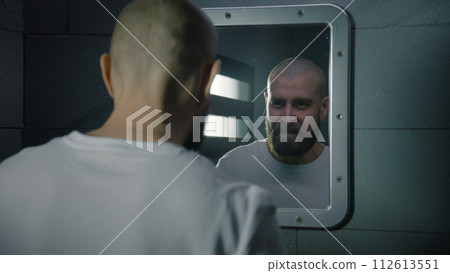 Male criminal wipes his face with towel and looks seriously in the mirror Male criminal wipes his face with towel and looks seriously in the mirror 112613551