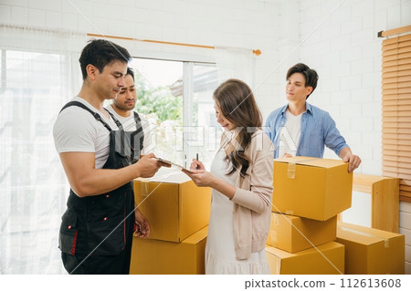 Family reviews moving checklist worker holds a delivery box. Professional movers ensure a successful home relocation. Teamwork and efficient moving displayed. Movind Day to New home 112613608
