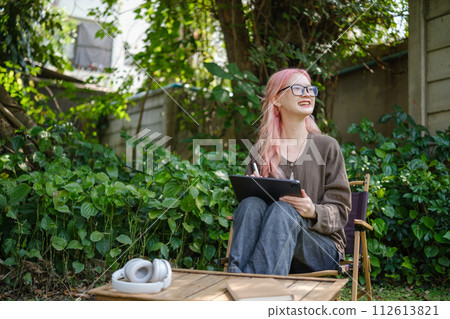 Cute pink hair girl drawing on digital tablet in garden, Woman Doing Freelance Work in Garden, woman with digital tablet with artwork. Cute pink hair girl drawing on digital tablet in garden, Woman Doing Freelance Work in Garden, woman with digital tablet with artwork. 112613821