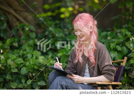 Cute pink hair girl drawing on digital tablet in garden, Woman Doing Freelance Work in Garden, woman with digital tablet with artwork. 112613823