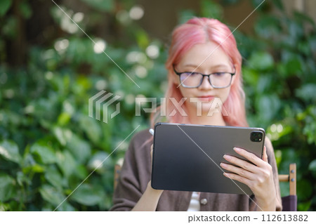 Cute pink hair girl drawing on digital tablet in garden, Woman Doing Freelance Work in Garden, woman with digital tablet with artwork. 112613882