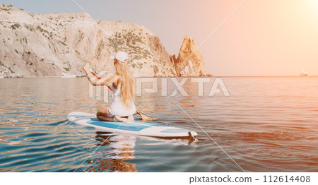 Woman sea sup. Close up portrait of happy young caucasian woman with long hair looking at camera and smiling. Cute woman portrait in bikini posing on sup board in the sea Woman sea sup. Close up portrait of happy young caucasian woman with long hair looking at camera and smiling. Cute woman portrait in bikini posing on sup board in the sea 112614408