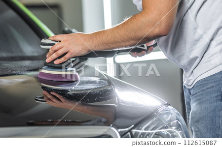 Young man polishing the hood of the car with an orbital polisher for removing scratches from the car, detailing concept Young man polishing the hood of the car with an orbital polisher for removing scratches from the car, detailing concept 112615087
