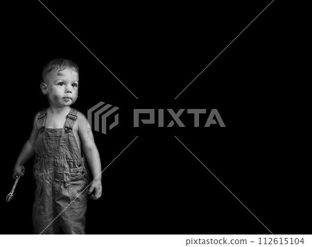 little boy in overalls with a wrench on a black background 112615104