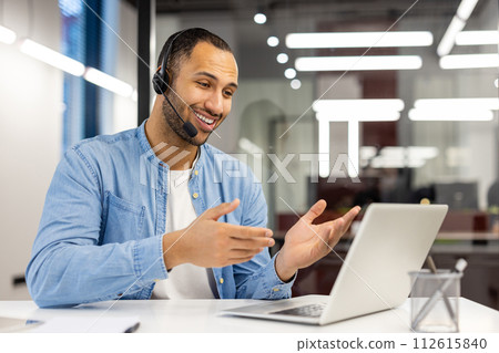 A focused professional engages in a video call using his laptop and headphones in a modern office setting. A focused professional engages in a video call using his laptop and headphones in a modern office setting. 112615840